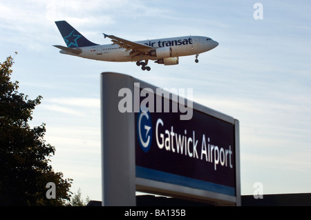 Die Landung-Räder sind unten als ein Air Transat kanadischen Jet-Flugzeug über dem Bahnhof am Flughafen London Gatwick landet Stockfoto