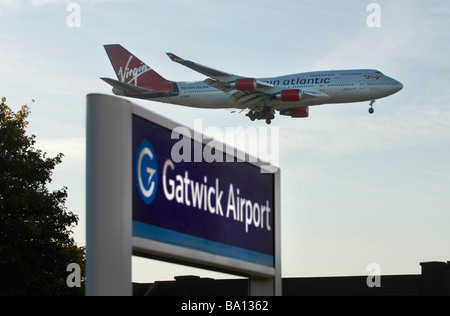 Die Landung-Räder sind unten als eine Virgin Atlantic Jet-Flugzeug über dem Eisenbahn-Bahnhof-Schild am Flughafen Gatwick landet. Stockfoto