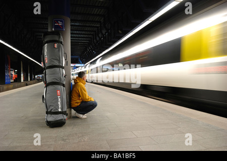 Ein Passagier mit Wintersport Gepäck wartet auf der Plattform am Zürich Flughafenbahnhof Zug als ein verschwommenes Zug Stockfoto