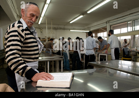Ein religiöser jude betet, während andere Juden Matzot traditionell vorbereiten Ungesäuertes Brot, das am Passahfest in der Kfar Chabad Bäckerei gegessen wird Zentralisraelisch Stockfoto