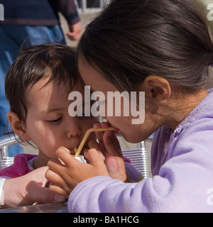 Zwei junge halb-Thai-Schwestern auf ihre Sommerferien trinken aus der gleichen Milchshake-Flasche durch Strohhalme Stockfoto