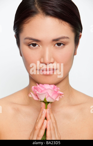 Studioaufnahme von eine schöne junge japanische Frau hält eine rosa Rose zwischen den gefalteten Händen in der meditativen Betrachtung Stockfoto