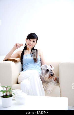 Junge Frau sitzt mit Wire Fox Terrier auf Sofa wegschauen mit Stift in den Zähnen Stockfoto