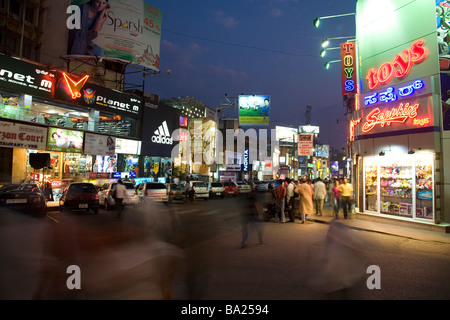 Abend auf Brigade Road im Zentrum von Bangalore, Indien. Fassaden mit Handelsnamen und Werbung Werbetafeln. Stockfoto