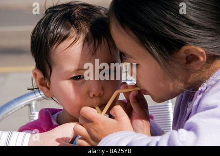 Zwei junge halb-Thai-Schwestern auf ihre Sommerferien trinken aus der gleichen Milchshake-Flasche durch Strohhalme Stockfoto