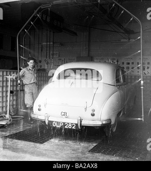 1950s, Autowäsche, ein männlicher Angestellter, der ein Auto aus Austin der Zeit beaufsichtigt, das von einer Reihe von Jets auf einem Rohr an einer Tankstelle in England, Großbritannien, gewaschen wurde. Stockfoto