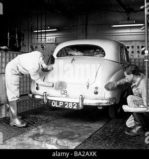 In den 50er Jahren, historisch, wischen zwei uniformierte Wartungspersonden ein Auto aus der Zeit von Austin nach dem Waschen trocken, England, Großbritannien. Stockfoto