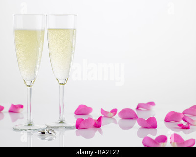 Zwei Trauringe neben Champagner-Flöten und Rosenblüten Stockfoto