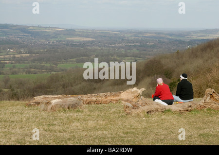 Zwei Frauen Wanderer sitzen auf einem Baumstamm, genießen den Blick auf einen nebligen Sussex Weald von der South Downs Way, West Sussex, England Stockfoto