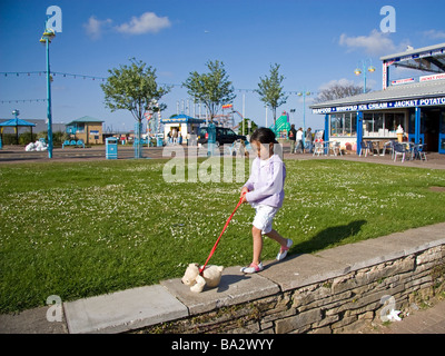 Ein halb-Thai-Mädchen geht einen Spielzeughund entlang der Brüstung eine kleine Mauer an einem sonnigen Sommertag in Skegness Stockfoto