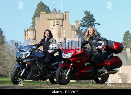 Zwei weibliche Motorradfahrer posiert mit Fahrräder tragen von Schutzkleidung an schottischen Schloss Ort Stockfoto