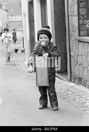 70er Jahre, schwarz / weiß Foto, Menschen, Kinder, kleiner Junge mit einem Ratch oder Rassel, Apfel in den Mund, im Alter von 4 bis 7 Jahre, Osterbräuche in der Eifel, in der Karwoche in ländlichen Gebieten Kinder herumlaufen mit Ratches oder Rasseln, symbolisch diese Raspeln oder Klappern soll das Läuten der Glocken ersetzen, weil in der Karwoche alle Glocken nach Rom gereist , D-Monreal, Elz, Elzbach, Elztal, Eifel, Verbandsgemeinde Vordereifel, Rheinland-Pfalz Stockfoto