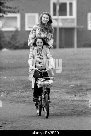 70er Jahre, schwarz / weiß Foto, Menschen, zwei junge Mädchen fahren auf ein Fahrrad, ein Mädchen steht am Koffer Rack, Humor, Spaß, im Alter von 18 bis 22 Jahre Stockfoto