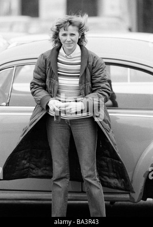 Achtziger Jahre, schwarz / weiß Foto, Menschen, junge Frau steht steht vor ein Auto, Pulli, Mantel, Jeans Hosen, im Alter von 30 bis 35 Jahre, Kriemhild Stockfoto