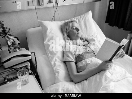 Achtziger Jahre, schwarz / weiß Foto, Menschen, Gesundheit, junge Frau liegt in einem Krankenbett eines Krankenhauses, ein Buch lesen, im Alter von 30 bis 40 Jahre, Elisabeth Stockfoto