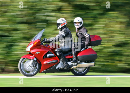 Rot Motorrad mit männlichen Fahrer in schwarzem Leder und weiblichen Sozius-beide tragen Helme auf Landstraße Stockfoto