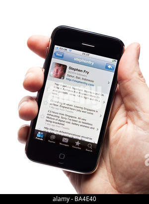 Männliche Hand, die iPhone zeigt Tweets von Stephen Fry ein produktiver Promi-Twitter-fan Stockfoto