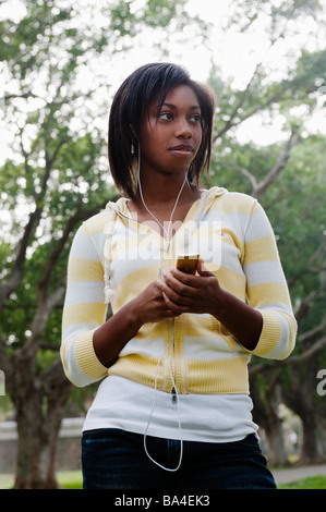 Junge Frau im Park stehen anhören von Musik auf MP3-Player Stockfoto