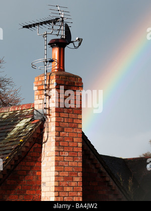 ein Regenbogen hinter einen Schornstein mit Fernsehantennen in hellem Sonnenlicht Stockfoto