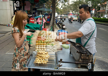 Ein junges thailändisches Mädchen, das die berühmten Bangkoker Fleischspieße aus einem Straßenstall wählt Stockfoto