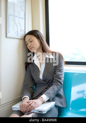 Geschäftsfrau mit Laptop am Oberschenkel Augen ruhen auf Zug sitzt Stockfoto