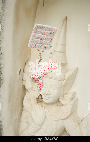 Ein rotes gefleckte Papier Angebot hängt vor einer Tempelwand Schnitzen in Bangkok Thailand Stockfoto