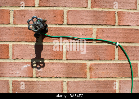 elektrischer Draht auf eine Mauer aus einer externen Wasserhahn laufen Stockfoto