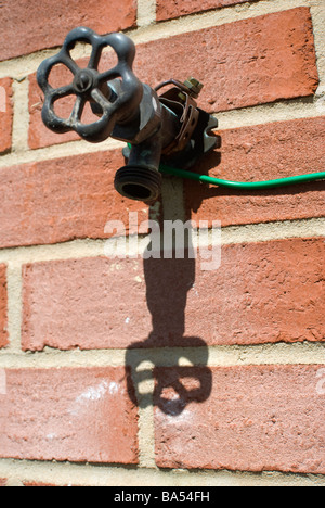 elektrischer Draht auf eine Mauer aus einer externen Wasserhahn laufen Stockfoto