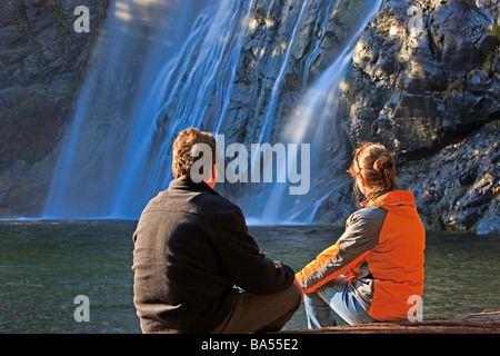 Paar sitzt auf einem Baumstamm Anzeigen der Jungfrau fällt die 53 m 174 Füße in einer Fan-Formation stürzen hinunter einen Felsen Escarpment. Stockfoto