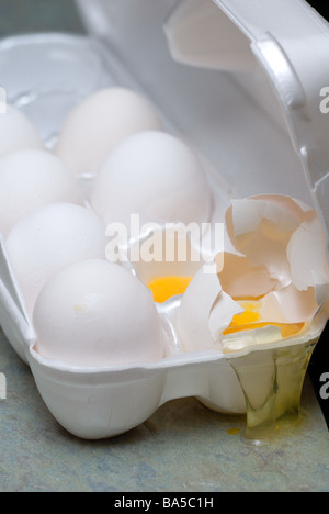 Eigelb schwappt von einem gebrochenen Ei in eine offene Eierkarton. Stockfoto