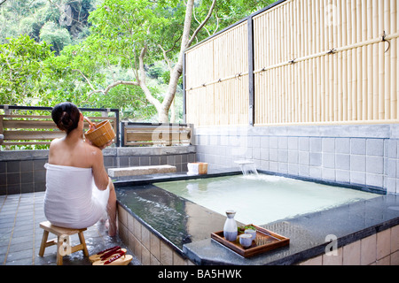 Junge Frau im Badetuch auf Stuhl sitzend mit Kelle in der hand von hinten Blick auf den pool Stockfoto