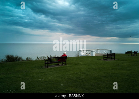 Eine alte Dame sitzt Blick auf das Meer an einem kühlen, ruhigen Abend im Frühjahr Stockfoto