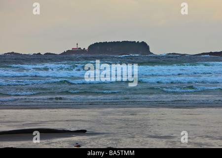 Stürmische Wellen des Pazifischen Ozeans am Strand von Cox Bay in der Nähe von Tofino mit dem Lennard-Insel-Leuchtturm im Hintergrund, ein tr Stockfoto