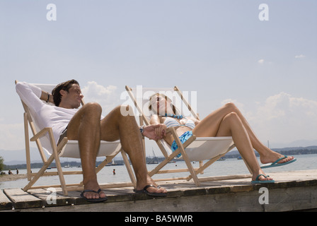 Meer-Holz-Brücke paar Liegestühle relaxen Blick-Kontakt Hände Lächeln hält Serie Leute Meeresküsten Kies Strand Liebe-sitzt Stockfoto