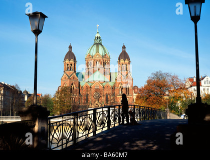 Frau mit Hund stehen auf der Kabetsteg Steg mit St. Lucas Church im Hintergrund München Bayern Deutschland Stockfoto