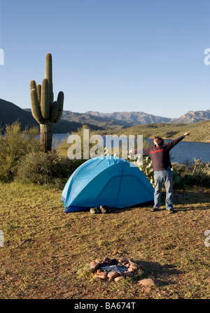 Ein Mann gähnt und erstreckt sich beim camping allein bei Sonnenaufgang auf einer Klippe mit Blick auf Apache Lake Arizona Stockfoto