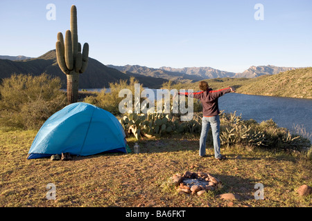 Ein Mann gähnt und erstreckt sich beim camping allein bei Sonnenaufgang auf einer Klippe mit Blick auf Apache Lake Arizona Stockfoto