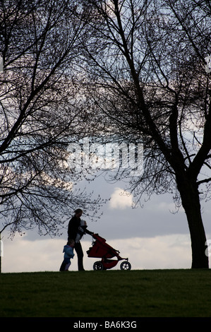 Beschäftigt Mutter einen Buggy zu schieben, während die Hand des Kindes Kleinkind und ein Baby im Tragetuch tragen Stockfoto