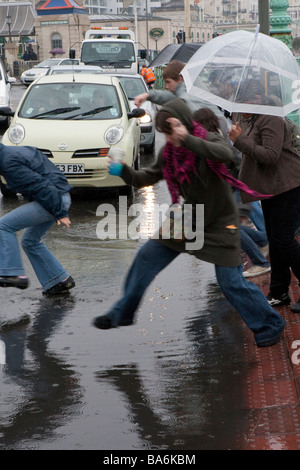 Menschen springen in Pfützen des Regenwassers in überfluteten Straße, Palace Pier, Brighton Stockfoto