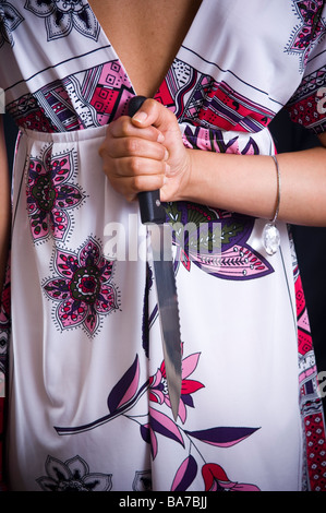 Frau mit einem Küchenmesser hinter ihrem Rücken Stockfoto