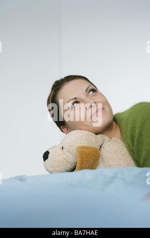 Junge Frau hält einen ausgestopften Hund auf Bett, München, Deutschland Stockfoto