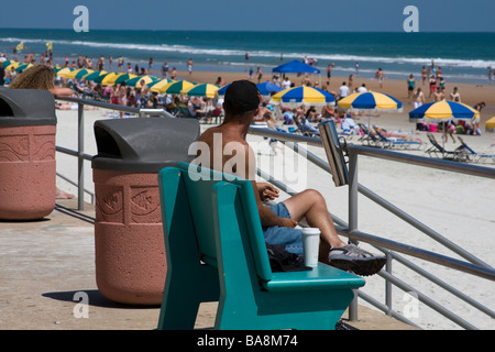 Eine andere Arbeit und möglicherweise Obdachloser sitzt auf einer Bank an einer Promenade auf der verzweifelten Suche. Stockfoto