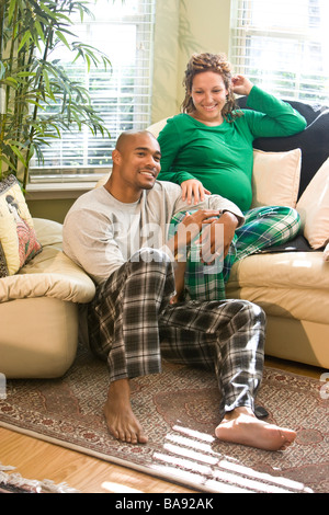 African-American Paar sitzt im Wohnzimmer tragenden Pyjamas, Frau schwanger Stockfoto