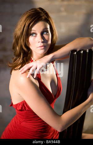 Porträt der jungen Frau im roten Kleid sitzt im Lager Stockfoto