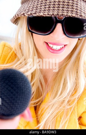 lächelnde Frau mit Sonnenbrille hält mic Stockfoto