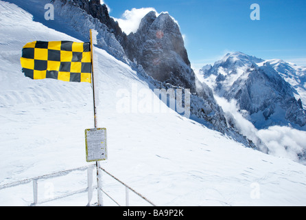 Lawinenwarnflagge (4/5, hohes Risiko) auf dem Gipfel von Grands Montets, Chamonix, Frankreich. Das Mont Blanc Massiv ist im Hintergrund zu sehen. Stockfoto