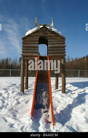 Ein Blockhaus und Folie auf einem Spielplatz in der First Nation Ortschaft Old Crow, Yukon Territorium, Kanada. Stockfoto