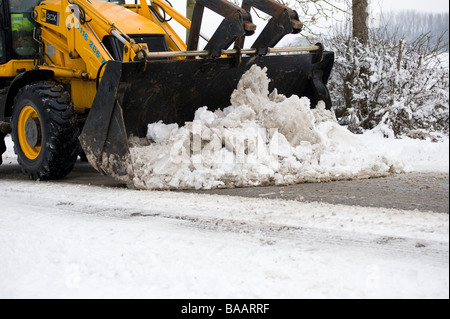 JCB mit Schaufel Eimer wird verwendet, um eine Schnee bedeckt Straße auf dem Land in England im winter Stockfoto