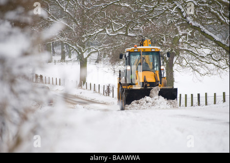 JCB wird verwendet, um eine Schnee bedeckt Straße auf dem Land in England im winter Stockfoto