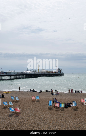 Blick über einen Kiesstrand, übersät mit Liegestühlen in Richtung Brighton Pier. Stockfoto